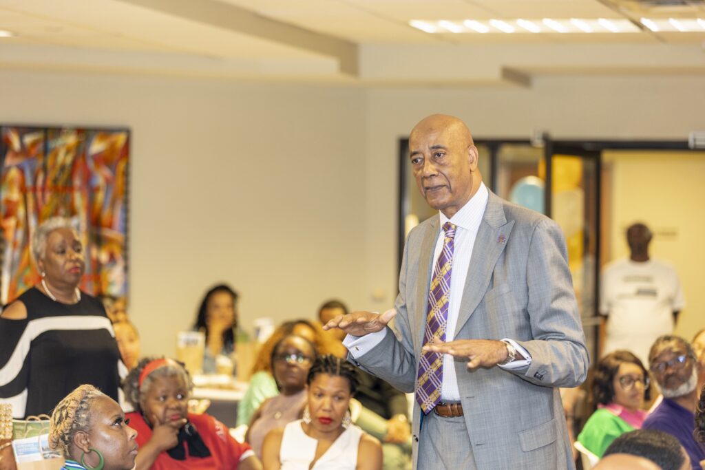 Dr. Joseph Webb speaking to a seated community audience, gesturing as he explains a point